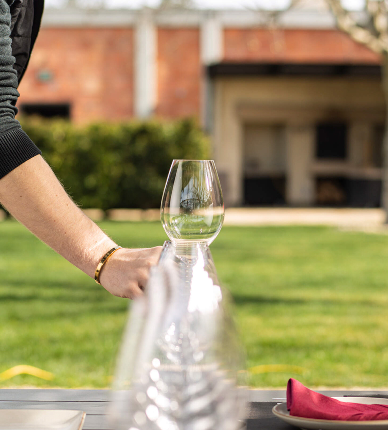 Person placing a wine glass next to other wine glasses on a table outdoors.
