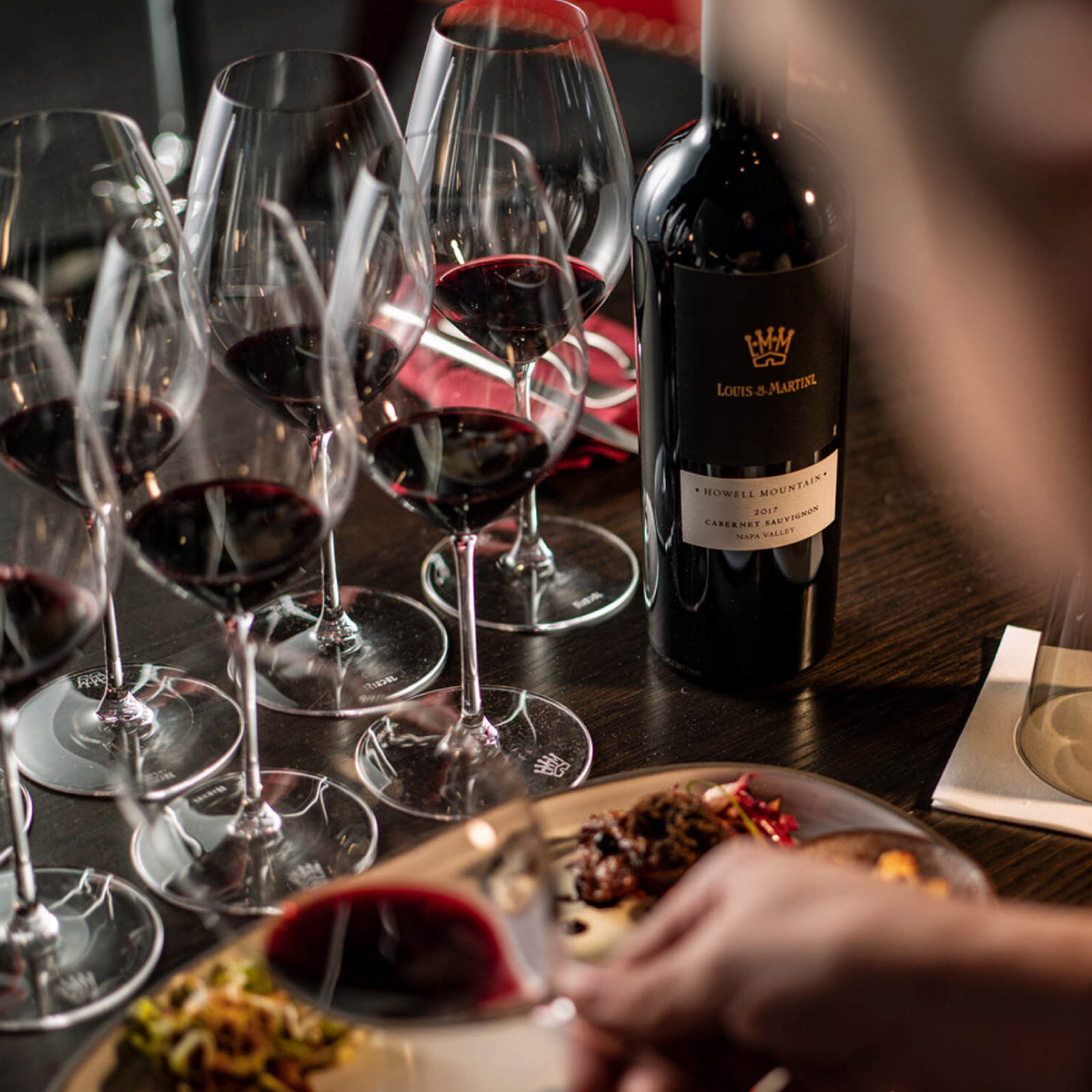 Numerous glasses filled with red wine, alongside food.